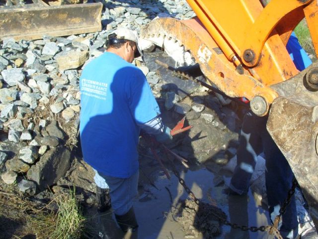 The hook used to grab pieces of the clog.  Next to his feet is a lump of mud, roots and trash that was pulled out.  The excavator did the pulling. 